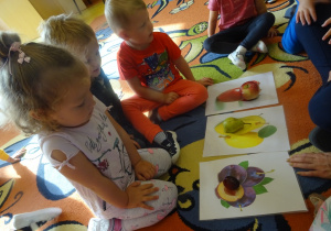 Dzieci siedzą wokół ilustracji i dopasowanymi do nich owocami.