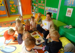 Grupa dzieci siedzi na dywanie wokół pani Eweliny, która prezentuje plansze z kolorem żółtym.