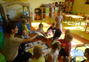 Dzieci siedzą na dywanie, Pani Ewelina podaje plansze z figurą chłopcu.