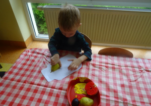 Chłopiec stempluje owocami papierowy szablon słoika.