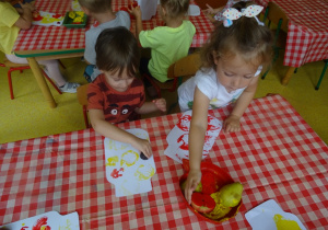 Dwoje dzieci stempluje owocami papierowy szablon słoika.