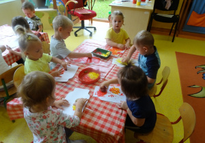 Sześcioro dzieci stempluje owocami papierowy szablon słoika.