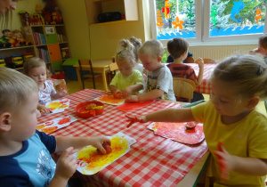 Pięcioro dzieci stempluje owocami papierowy szablon słoika.