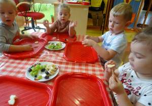 Czworo dzieci robi owocowe przekąski, nakładają małe kawałki owoców na wykałaczki.