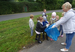 Kilkoro dzieci wrzuca śmieci do worka, który trzyma pani Agnieszka.