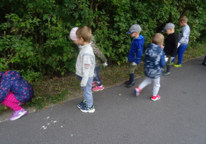 Grupa dzieci spaceruje z pochyloną głową w poszukiwaniu odpadów.