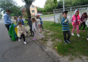 Dzieci zbierają śmieci z trawnika i wrzucają je do worków.