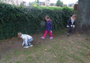 Troje dzieci zbiera śmieci z trawnika.