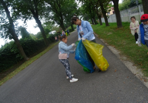 Dziewczynka wrzuca śmieci do worka, który trzyma pani Monika.