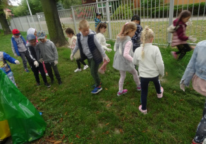 Grupa dzieci zbiera śmieci z trawnika.