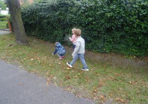 Troje dzieci spaceruje po trawniku i zbiera śmieci.