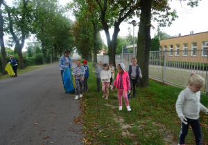 Grupa dzieci spaceruje po trawniku i zbiera śmieci. Pani Monika spaceruje wśród dzieci z workami.