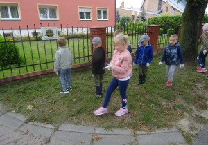 Grupa dzieci zbiera śmieci z trawnika.