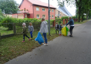 Dzieci zbierają śmieci z trawnika.