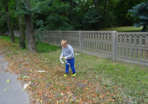 Chłopiec zbiera śmieci z trawnika.