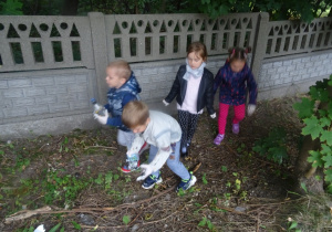 Czwórka dzieci zbiera śmieci pod płotem.