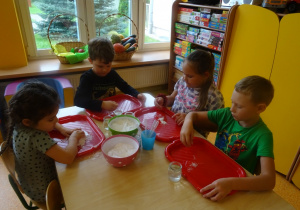 Dzieci wykonują doświadczenie z cieczą nienewtonowską, nasypują mąkę na tackę.