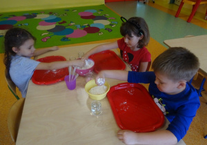 Dzieci wykonują doświadczenie z cieczą nienewtonowską, nasypują mąkę na tacki.