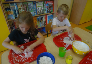Dzieci wykonują doświadczenie z cieczą nienewtonowską, mieszają mąkę z wodą na tackach.