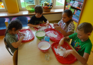 Dzieci wykonują doświadczenie z cieczą nienewtonowską, mieszają wodę z mąką na tackach.