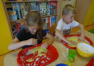Dzieci wykonują doświadczenie z cieczą nienewtonowską, barwią ją na żółto.