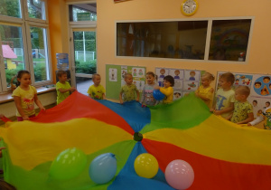 Dzieci trzymają za brzegi chustę animacyjną na której są ułożone balony.