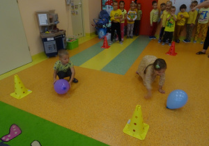 Dzieci turlają balona po podłodze.
