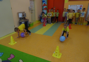 Dzieci turlają balona po podłodze.