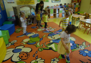 Dzieci przechodzą po śladach stóp rozłożonych na dywanie.