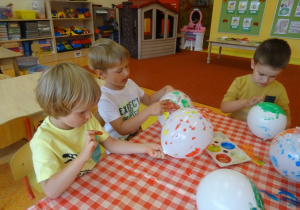 Dzieci malują paluszkami maczanymi w farbie balony.