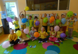 Grupa uśmiechniętych dzieci trzyma w ręku balony.