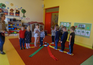 Dzieci bawią się wiatrakiem matematycznym, stoją na żółtych wstążkach. Pani Dorota gra na tamburynie.