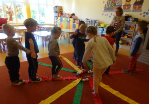 Dzieci bawią się wiatrakiem matematycznym, stoją na czerwonych wstążkach.