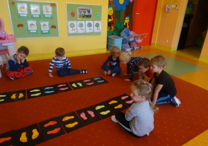 Dzieci siedzą wokół plansz z naklejonymi stopami w różnym kierunku.
