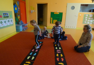 Dzieci chodzą po planszach z naklejonymi stopami.