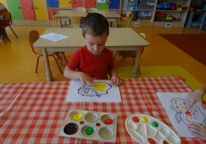 Chłopiec maluje gruszkę palcem.