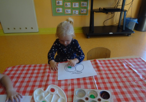 Dziewczynka maluje palcem kontur śliwki.