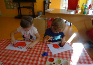 Dziewczynka maluje palcem jabłko, chłopiec śliwki.