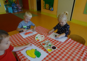 Dzieci malują palcami maczanymi w farbie owoce.