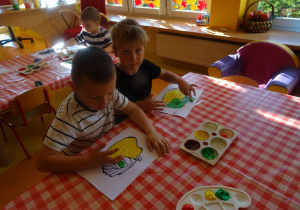 Dwóch chłopców maluje palcami maczanymi w farbie owoce.