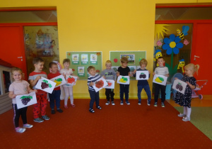 Dzieci stoją z kartkami na których są pomalowane owoce.