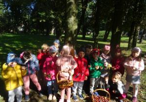 Grupa dzieci stoi w parku z zebranymi darami jesieni w koszykach.
