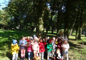 Grupa dzieci stoi w parku z zebranymi darami jesieni w koszykach. W tle drzewa.