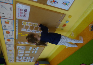 Dziewczynka koduje tabliczki z emocjami za pomocą cyfr na tablicy.
