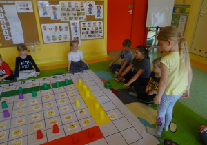 Dzieci grają w grę "Emocje" na macie edukacyjnej, dziewczynka rzuca kostką.