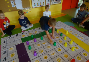 Dzieci grają w grę "Emocje" na macie edukacyjnej, chłopiec przestawia kubek na macie.