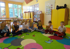 Dzieci siedzą w półkolu, oceniają stany emocjonalne za pomocą "mimicznych kopert", nałożonych na uniesioną rękę.