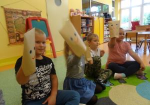 Dzieci siedzą w półkolu, oceniają stany emocjonalne za pomocą "mimicznych kopert", nałożonych na uniesioną rękę.