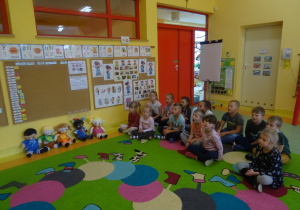 Dzieci oglądają film edukacyjny. Pod tablicą ułożone są laleczki z emocjami.