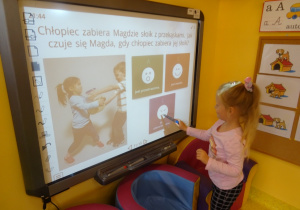 Dziewczynka rozwiązuje quiz na tablicy interaktywnej, unosi wskaźnik na właściwą odpowiedź.